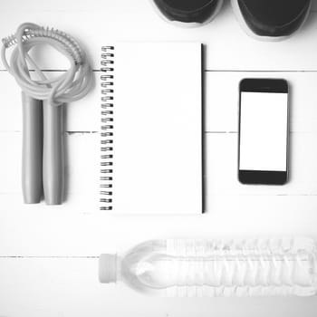 fitness equipment : running shoes,jumping rope,drinking water,notebook and phone on white wood table  black and white tone color style