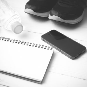 fitness equipment : running shoes,drinking water,notebook and phone on white wood table  black and white tone color style