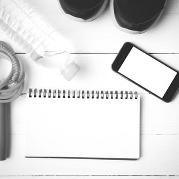 fitness equipment : running shoes,jumping rope,drinking water,notebook and phone on white wood table  black and white tone color style