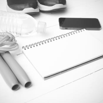 fitness equipment : running shoes,jumping rope,drinking water,notebook and phone on white wood table black and white tone color style