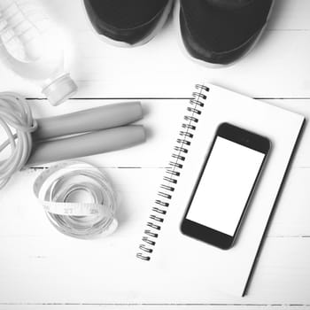 fitness equipment : running shoes,jumping rope,drinking water,notebook,measuring tape and phone on white wood table black and white tone color style