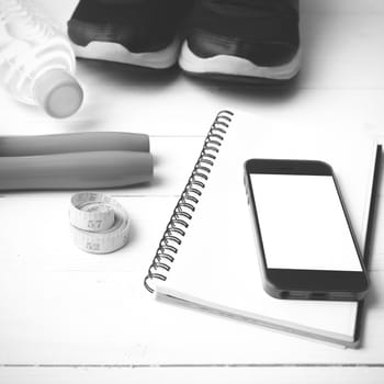 fitness equipment : running shoes,jumping rope,drinking water,notebook,measuring tape and phone on white wood table black and white tone color style