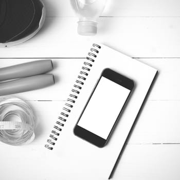 fitness equipment : running shoes,jumping rope,drinking water,notebook,measuring tape and phone on white wood table black and white tone color style