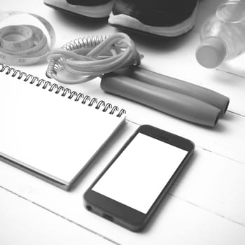 fitness equipment : running shoes,jumping rope,drinking water,notebook,measuring tape and phone on white wood table black and white tone color style