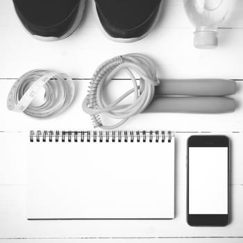 fitness equipment : running shoes,jumping rope,drinking water,notebook,measuring tape and phone on white wood table black and white tone color style