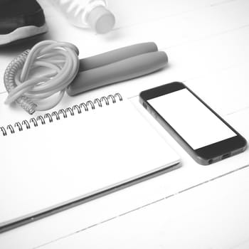 fitness equipment : running shoes,jumping rope,drinking water,notebook and phone on white wood table black and white tone color style