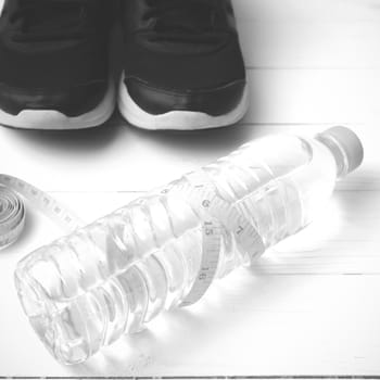 fitness equipment : running shoes,drinking water and measuring tape on white wood table black and white tone color style