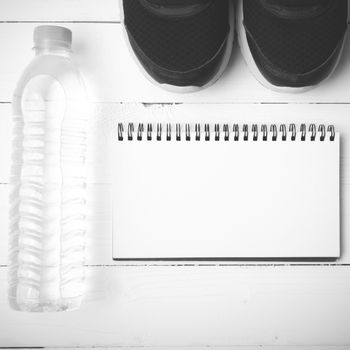 fitness equipment : running shoes,drinking water and notebook on white wood table black and white tone color style