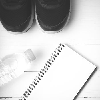 fitness equipment : running shoes,drinking water and notebook on white wood table black and white tone color style