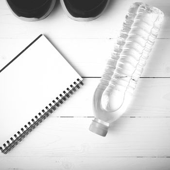 fitness equipment : running shoes,drinking water and notebook on white wood table black and white tone color style