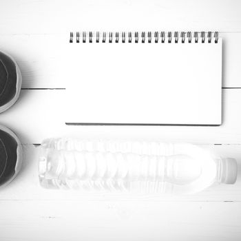 fitness equipment : running shoes,drinking water and notebook on white wood table black and white tone color style