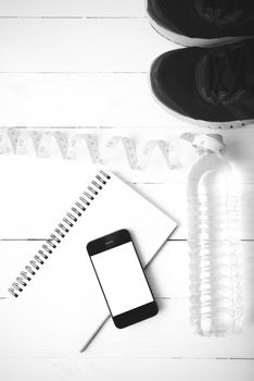 running shoes,measuring tape,drinking water,notebook and phone on white wood table black and white tone color style