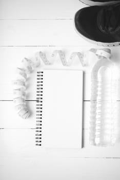 running shoes,measuring tape,drinking water and notebook on white wood table black and white tone color style