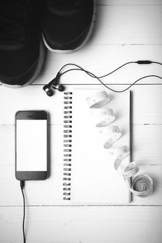 running shoes,measuring tape,notebook and phone on white wood table black and white tone color style