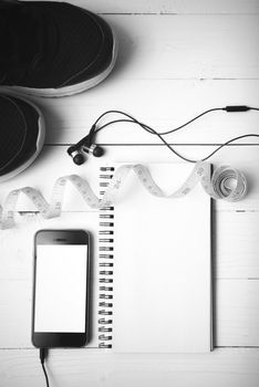 running shoes,measuring tape,notebook and phone on white wood table black and white tone color style