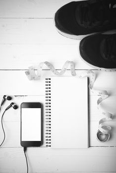 running shoes,measuring tape,notebook and phone on white wood table black and white tone color style