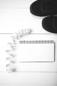 running shoes with notebook and measuring tape on white wood table black and white tone color style