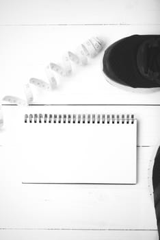 running shoes with notebook and measuring tape on white wood table black and white tone color style