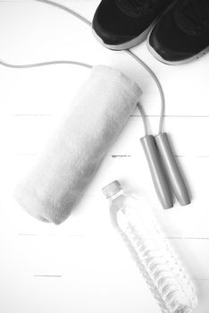 fitness equipment : running shoes,towel,jumping rope and drinking water on white wood table black and white color tone style