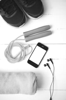 fitness equipment : running shoes,towel,jumping rope and phone on white wood table black and white color tone style