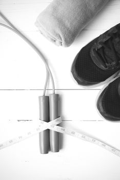 fitness equipment : running shoes,towel,jumping rope and measuring tape on white wood table black and white color tone style