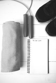 fitness equipment : running shoes,towel,jumping rope and notebook write to do list on white wood table black and white color tone style