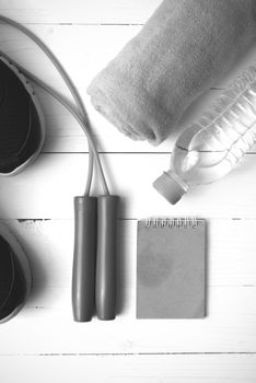 fitness equipment : running shoes,towel,jumping rope,water bottle and notepad on white wood table black and white color tone style