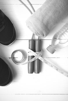 fitness equipment : running shoes,towel,jumping rope,water bottle and measuring tape on white wood table black and white color tone style