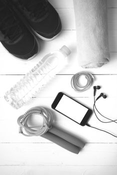 fitness equipment : running shoes,towel,jumping rope,water bottle,phone and measuring tape on white wood table black and white color tone style