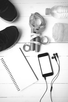 fitness equipment : running shoes,towel,jumping rope,water bottle,phone,notepad and measuring tape on white wood table black and white color tone style