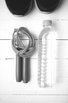 fitness equipment : running shoes,jumping rope and water bottle on white wood table black and white color tone style