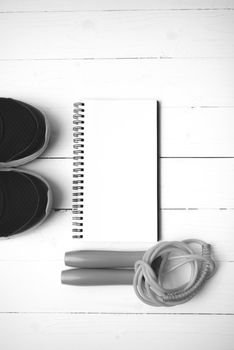 fitness equipment : running shoes,jumping rope and notepad on white wood table black and white color tone style