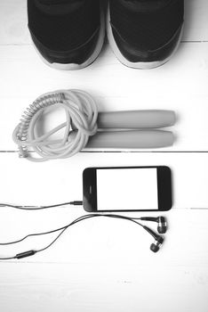 fitness equipment : running shoes,jumping rope and phone on white wood table black and white color tone style