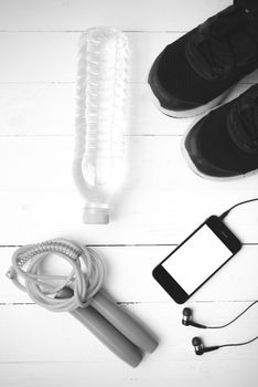 fitness equipment : running shoes,jumping rope,phone and water bottle on white wood table black and white color tone style