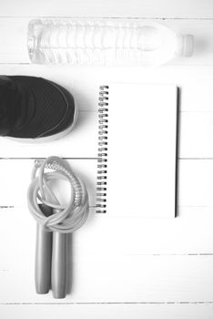 fitness equipment : running shoes,jumping rope,drinking water and notepad on white wood table  black and white tone color style