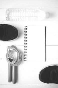 fitness equipment : running shoes,jumping rope,drinking water and notepad on white wood table  black and white tone color style