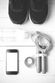 fitness equipment : running shoes,jumping rope,drinking water,measuring tape and phone on white wood table  black and white tone color style