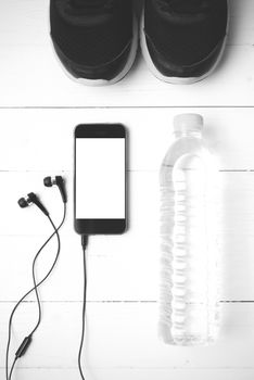 fitness equipment : running shoes,drinking water and phone on white wood table black and white tone color style