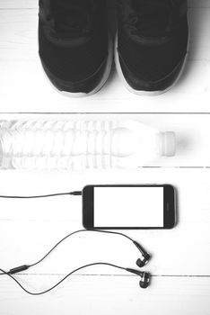 fitness equipment : running shoes,drinking water and phone on white wood table black and white tone color style