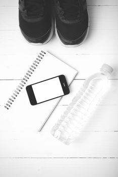 fitness equipment : running shoes,drinking water,notebook and phone on white wood table black and white tone color style