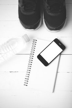 fitness equipment : running shoes,drinking water,notebook and phone on white wood table black and white tone color style