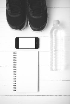 fitness equipment : running shoes,drinking water,notebook and phone on white wood table black and white tone color style