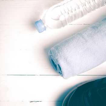 fitness equipment:blue towel,drinking water and running shoes on white wood table vintage style