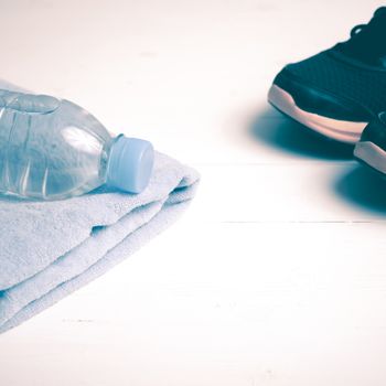 fitness equipment:blue towel,drinking water and running shoes on white wood table vintage style