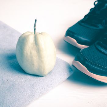 fitness equipment : running shoes,blue towel and guava fruit on white wood table vintage style