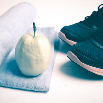 fitness equipment : running shoes,blue towel and guava fruit on white wood table vintage style