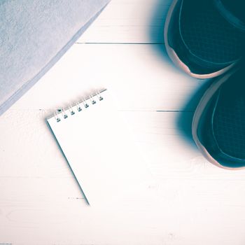 fitness equipment : running shoes,blue towel and notepad on white wood table vintage style