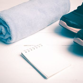fitness equipment : running shoes,blue towel and notepad on white wood table vintage style