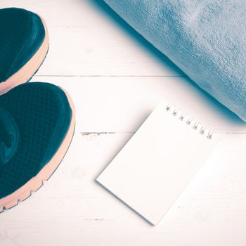 fitness equipment : running shoes,blue towel and notepad on white wood table vintage style