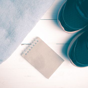 fitness equipment : running shoes,blue towel and notepad on white wood table vintage style